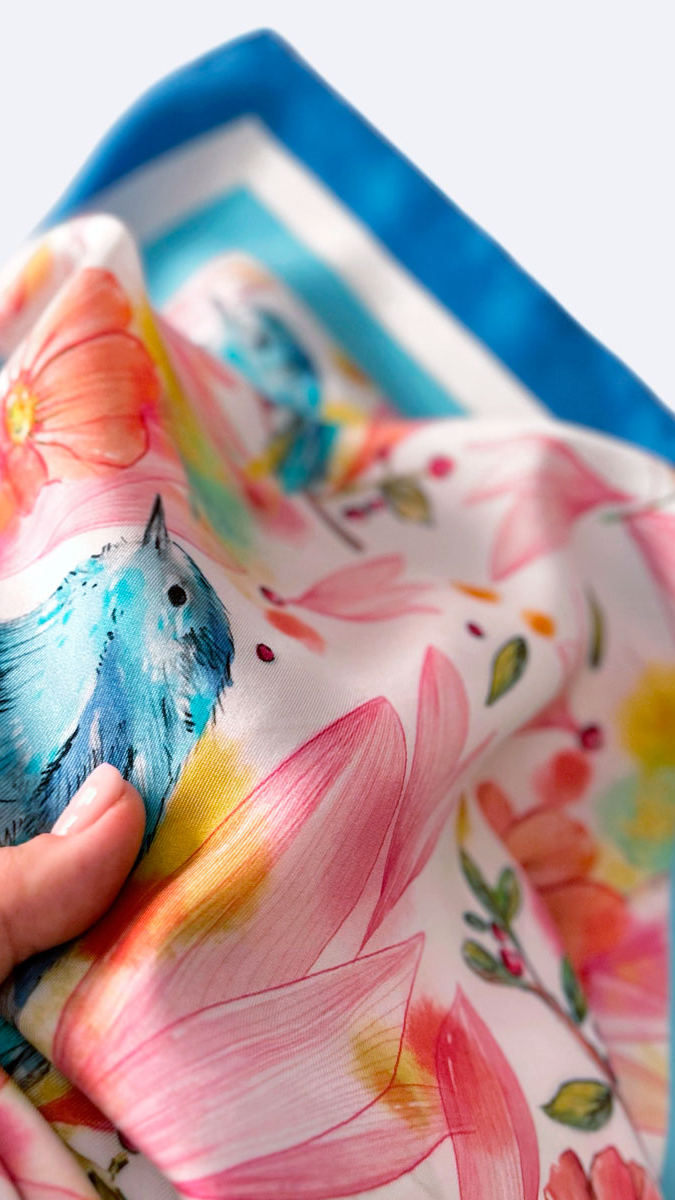 detalle de mano sosteniendo pañuelo de seda con ilustración de flores y pájaros