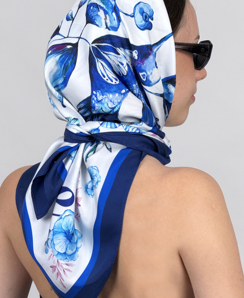 Side view of a woman with sunglasses and an illustrated blue and white silk scarf tied at the nape of her neck, classic luxury fashion