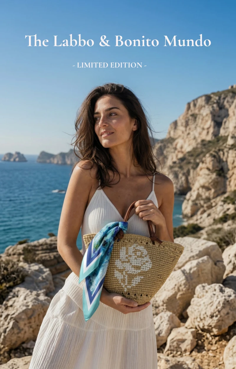 mujer con look en blanco sosteniendo mini capazo hecho a mano con panuelo de seda natural artesanal anudado en el asa cerca del mar